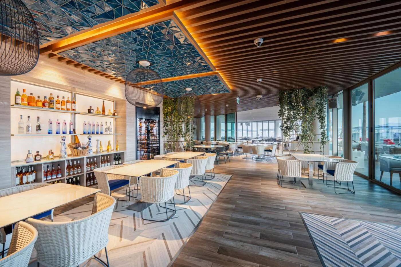 Modernes Restaurant mit Tischen, Stühlen, Bar und dekorativen Pflanzen. Helle Innenarchitektur mit Holz und Fliesen.