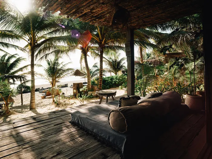 Habitación frente al mar en Nômade Tulum con área de asientos al aire libre con sombra de estilo cabaña, vista directa al mar y hermosas palmeras junto al mar.