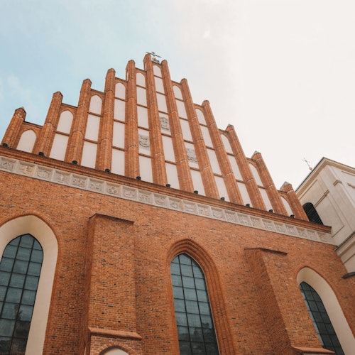 Gothic-style brick church facade with tall arched windows and vertical buttresses, viewed from a low angle.