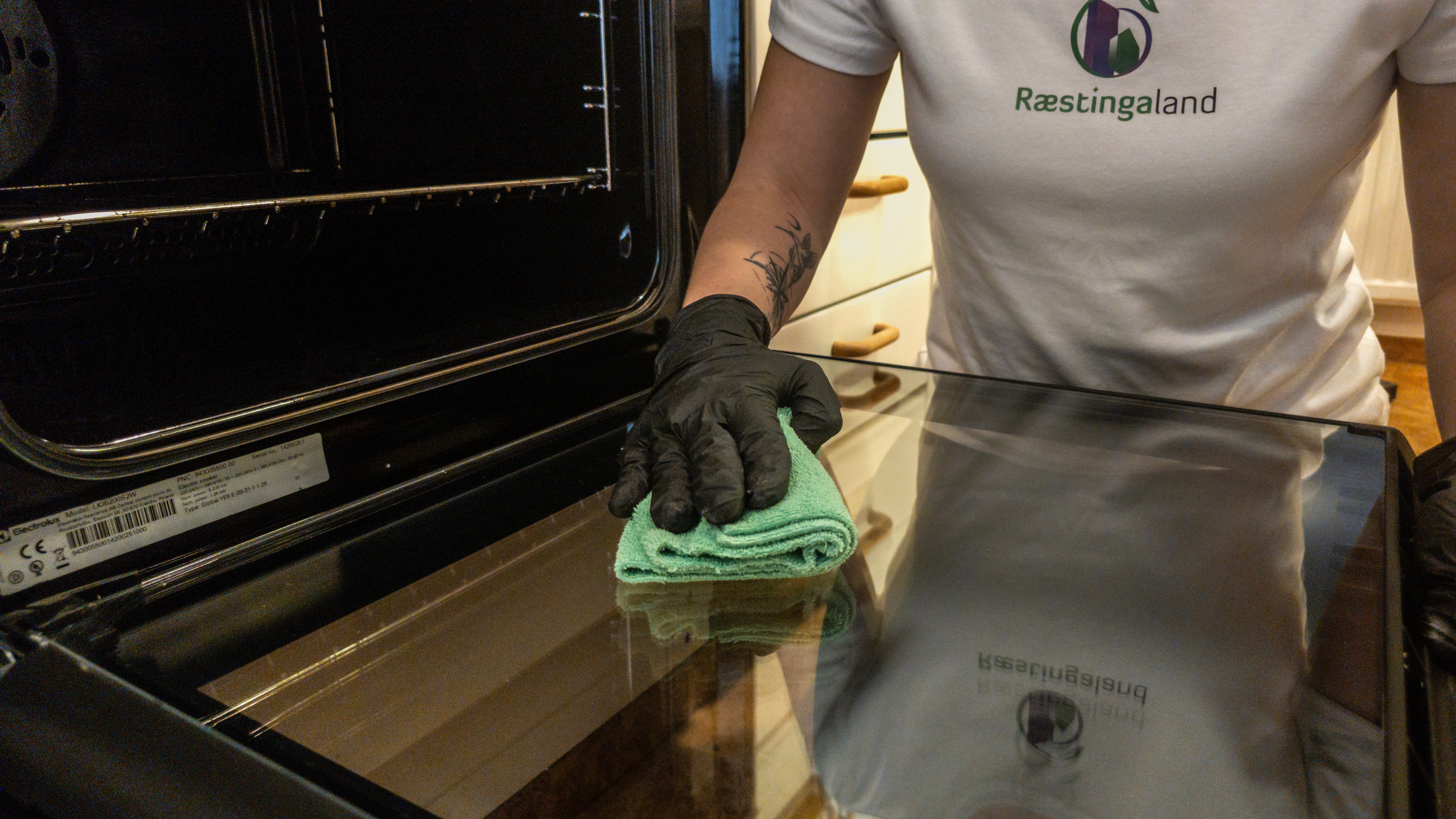 Starfsmaður Ræstingaland að þrífa ofnhurð og gler með örtrefjaklút.