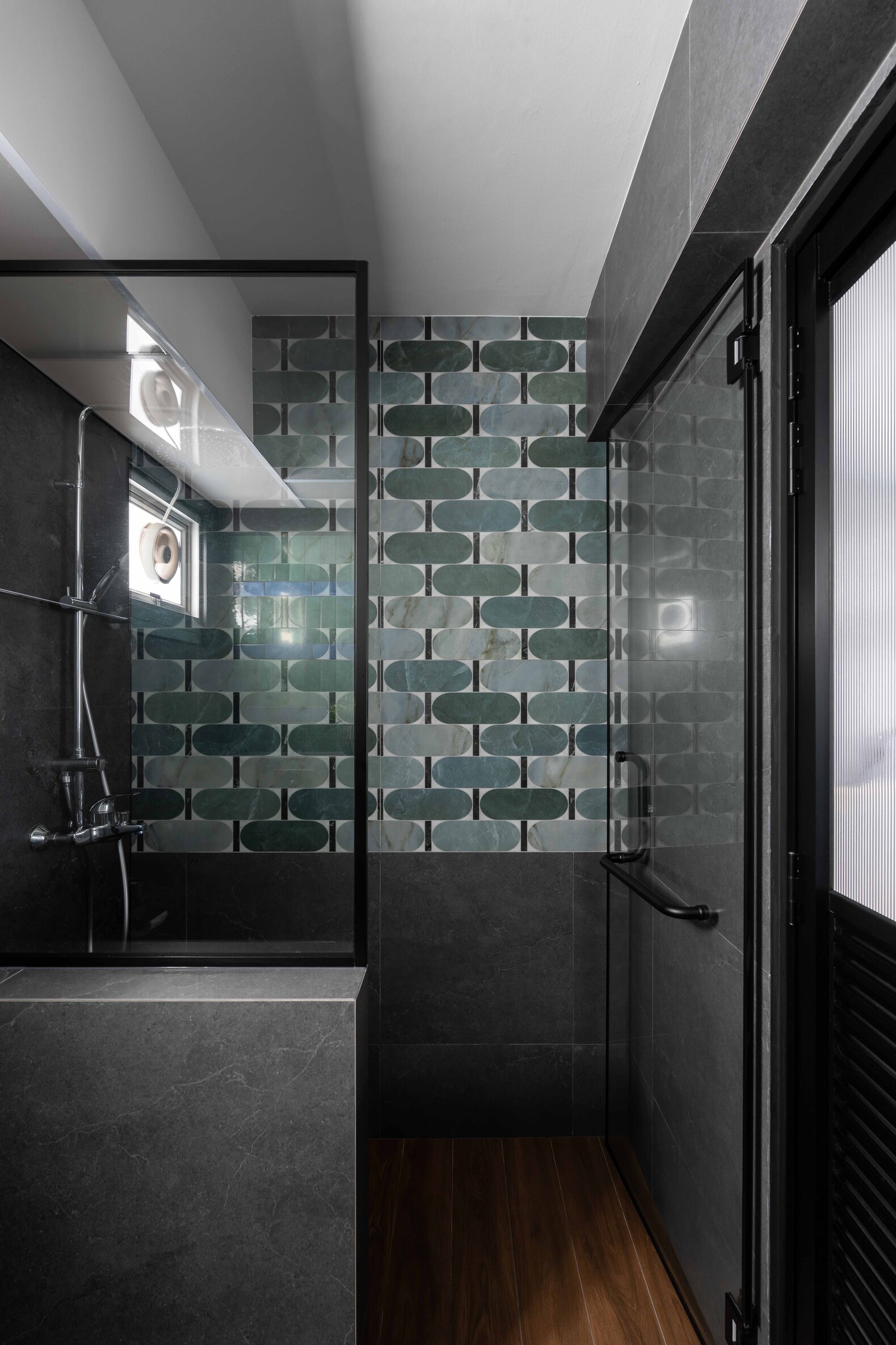 Modern bathroom featuring a glass shower, sleek dark tiles, and wood accents, with natural light filtering in.