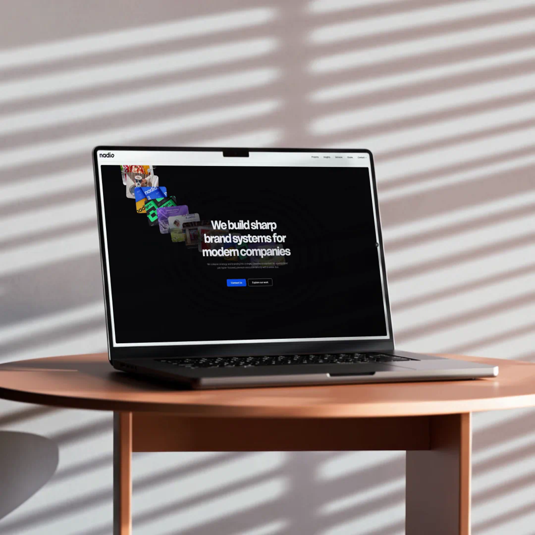Laptop mockup on a wooden table displaying the Nadio Studio homepage with bold agency positioning.