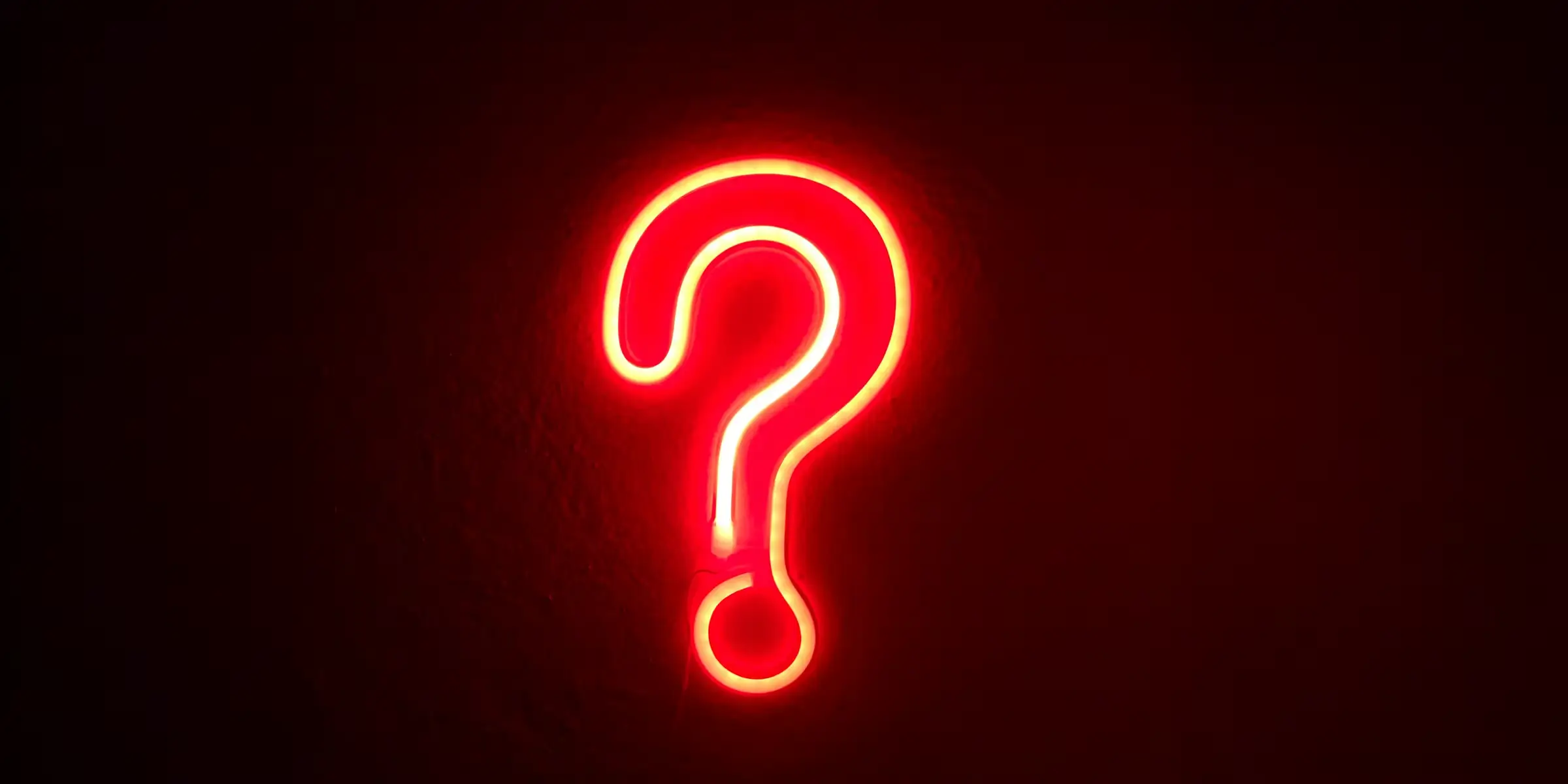 Neon red question mark glowing against a dark background, representing unanswered questions and the search for deeper insight.