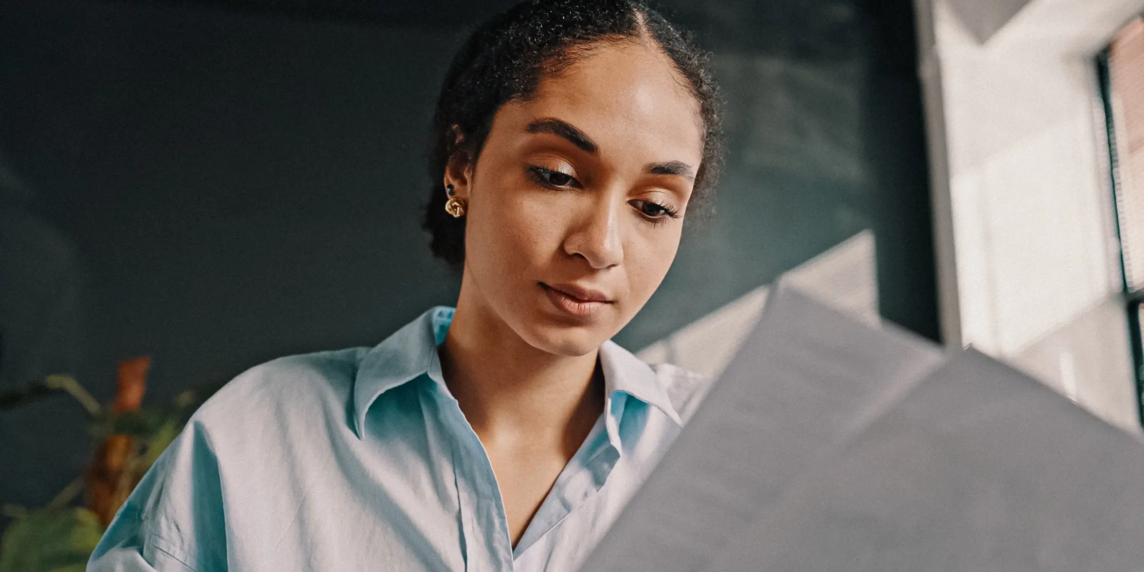 Legal associate reviewing case documents while wearing a light blue button-up shirt, with natural lighting and office greenery visible in background