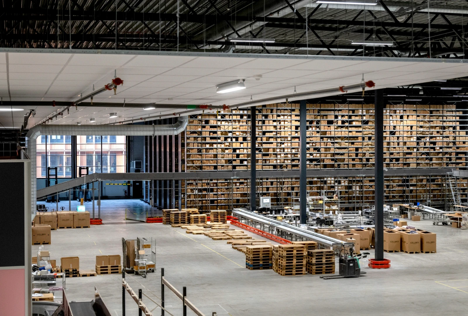En stor lagerlokal fylld med pallar och kartonger, med transportband och lastutrymmen.