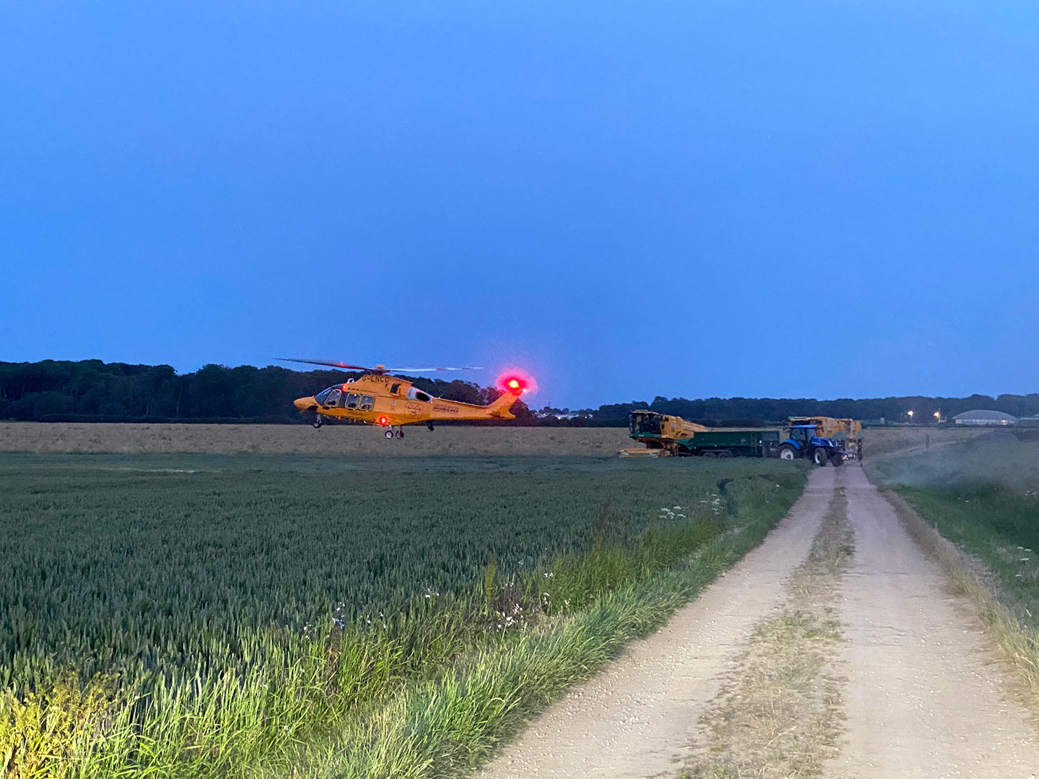 Yellow ambicopter with a red tail light taking off in a field. To the right are two farm vehicles.