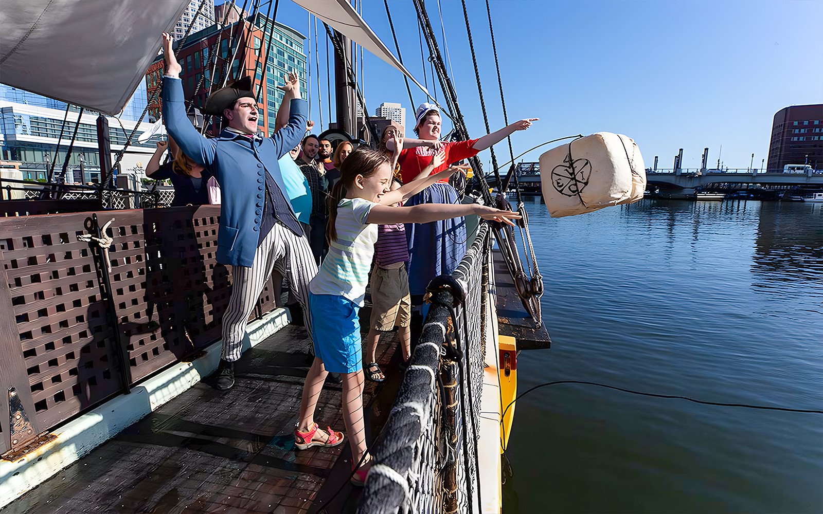 Tourists reenact Boston Tea Party by throwing tea chest from ship into harbor.