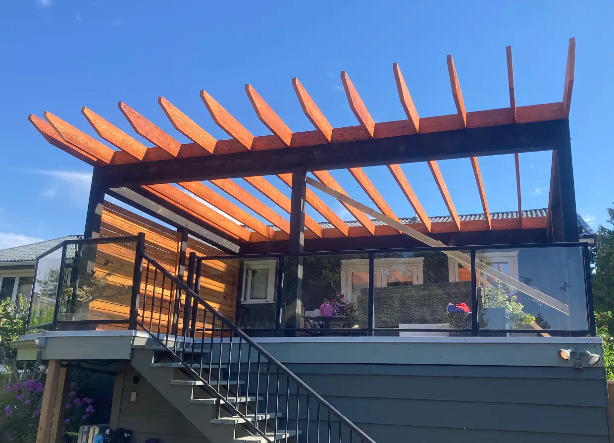 Custom backyard pergola built over raised deck with glass railing and outdoor living space.