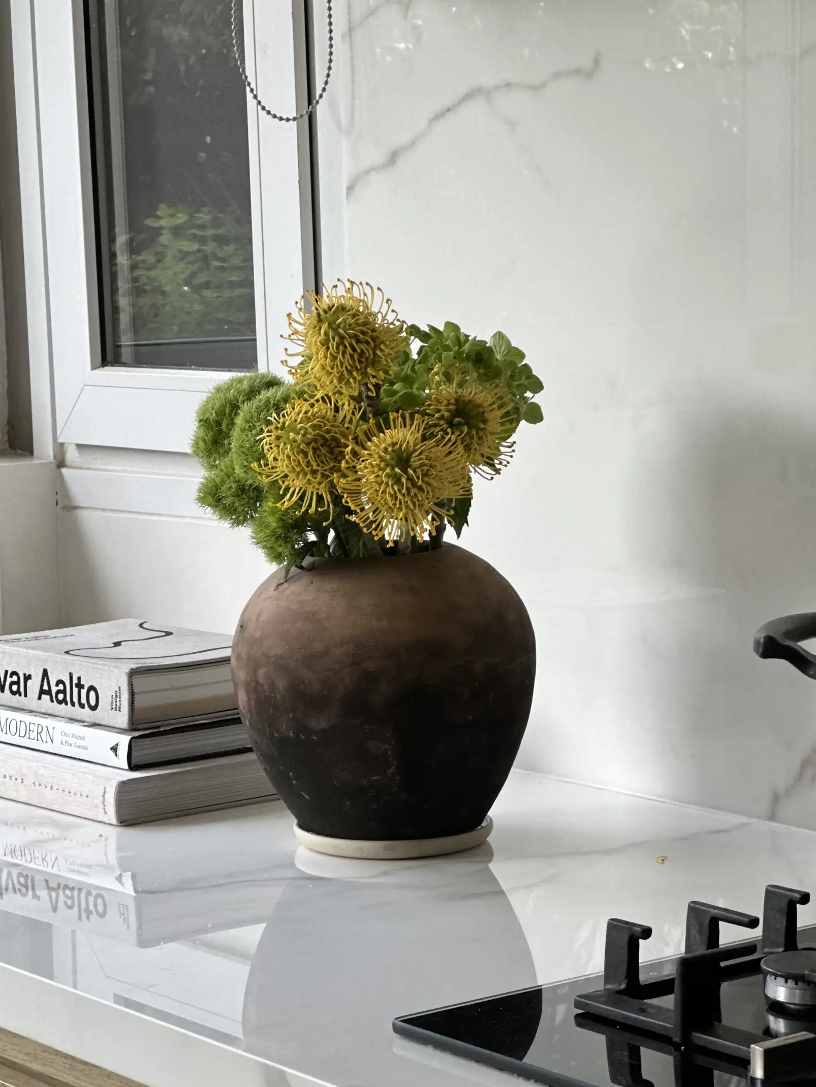 Arreglo floral amarillo en jarrón rústico sobre encimera de mármol para estilistas de interiores que combinan materiales naturales y contemporáneos.