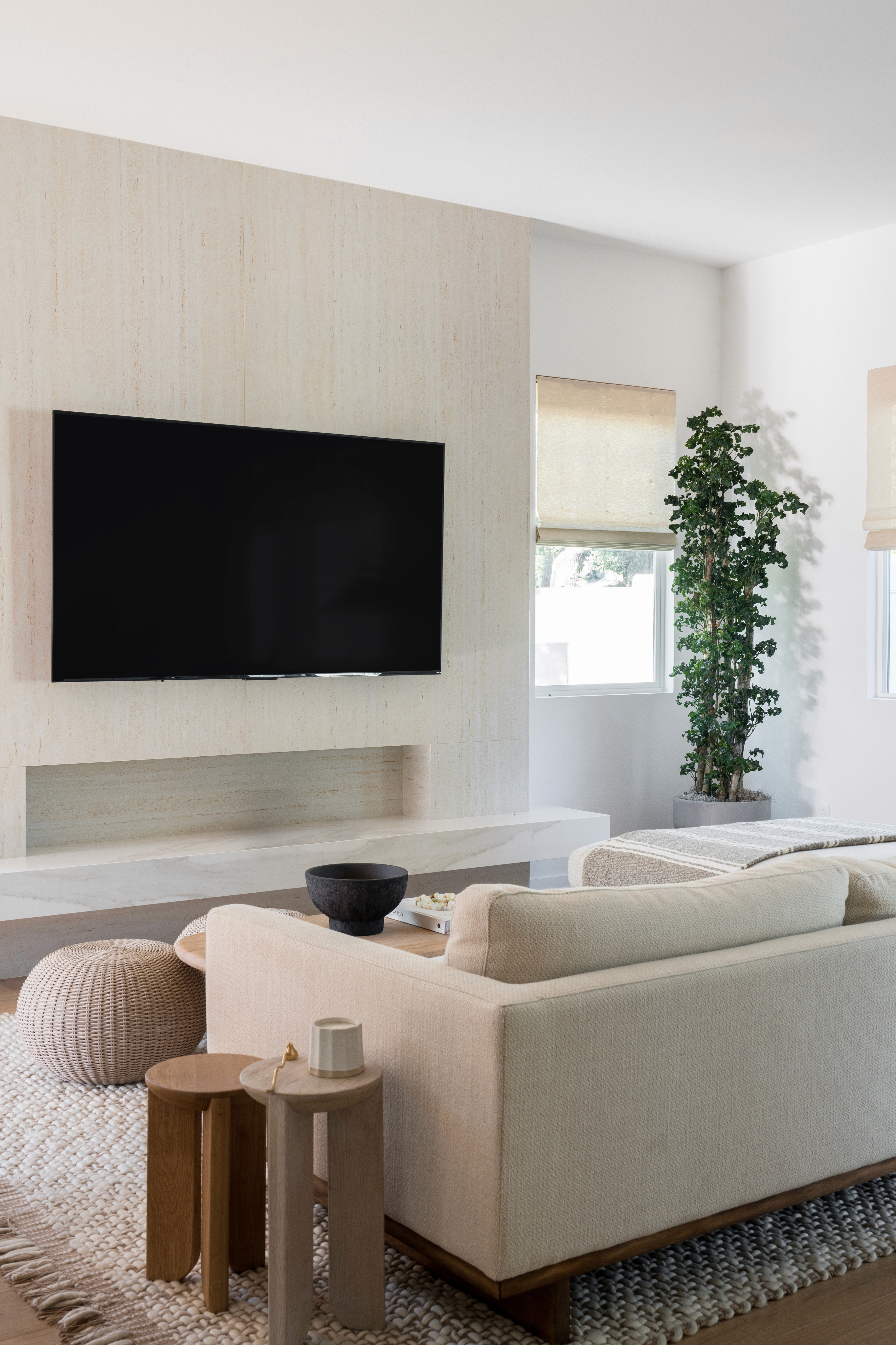 Living room with white linen couch, wood side tables, and rattan ottoman by Jubilee Interiors in Arcadia, California