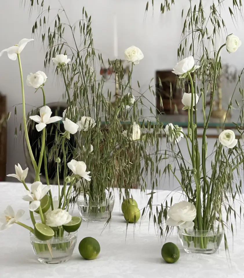 Centro de mesa con flores blancas, hojas de avena y limas frescas, composición minimalista y natural.