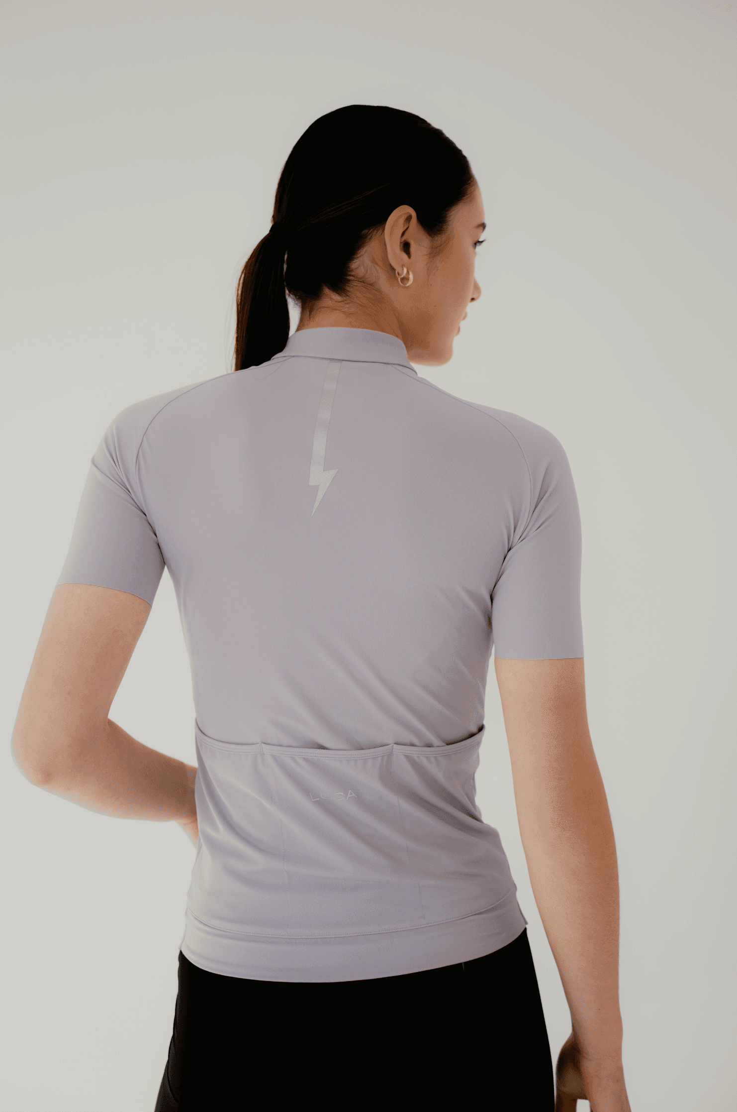 Back-view-of-a-woman-wearing-a-light-lavender-cycling-jersey-wth-a-reflctive-lighting-bolt-design-centered-below-the-collar-The-jersey-has-a-rear-pocket-line