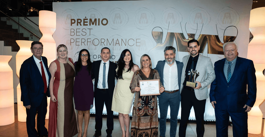 Executivos da PGMais posando com troféu ouro e certificado no palco do Prêmio Best Performance 2025