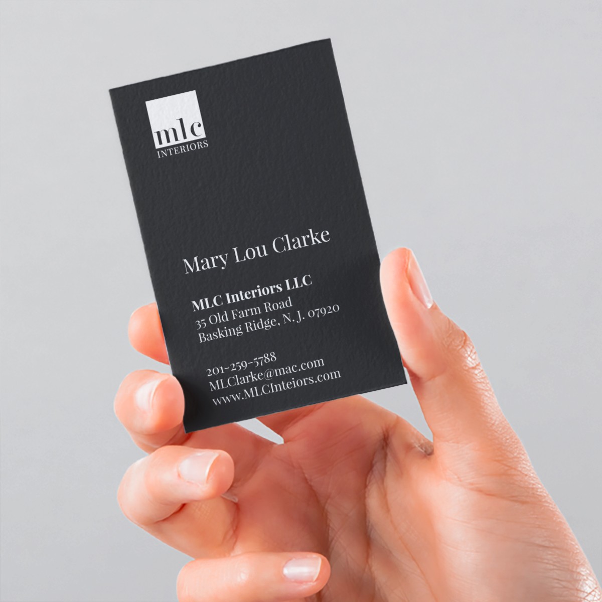 Hand holding a black MLC Interiors business card showing Mary Lou Clarke’s contact information.