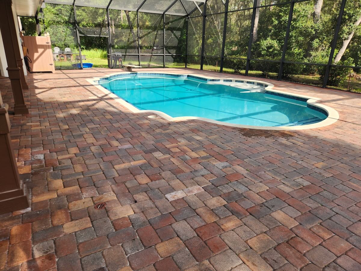 Before paver sealing - faded pool deck with weeds in Ormond Beach FL