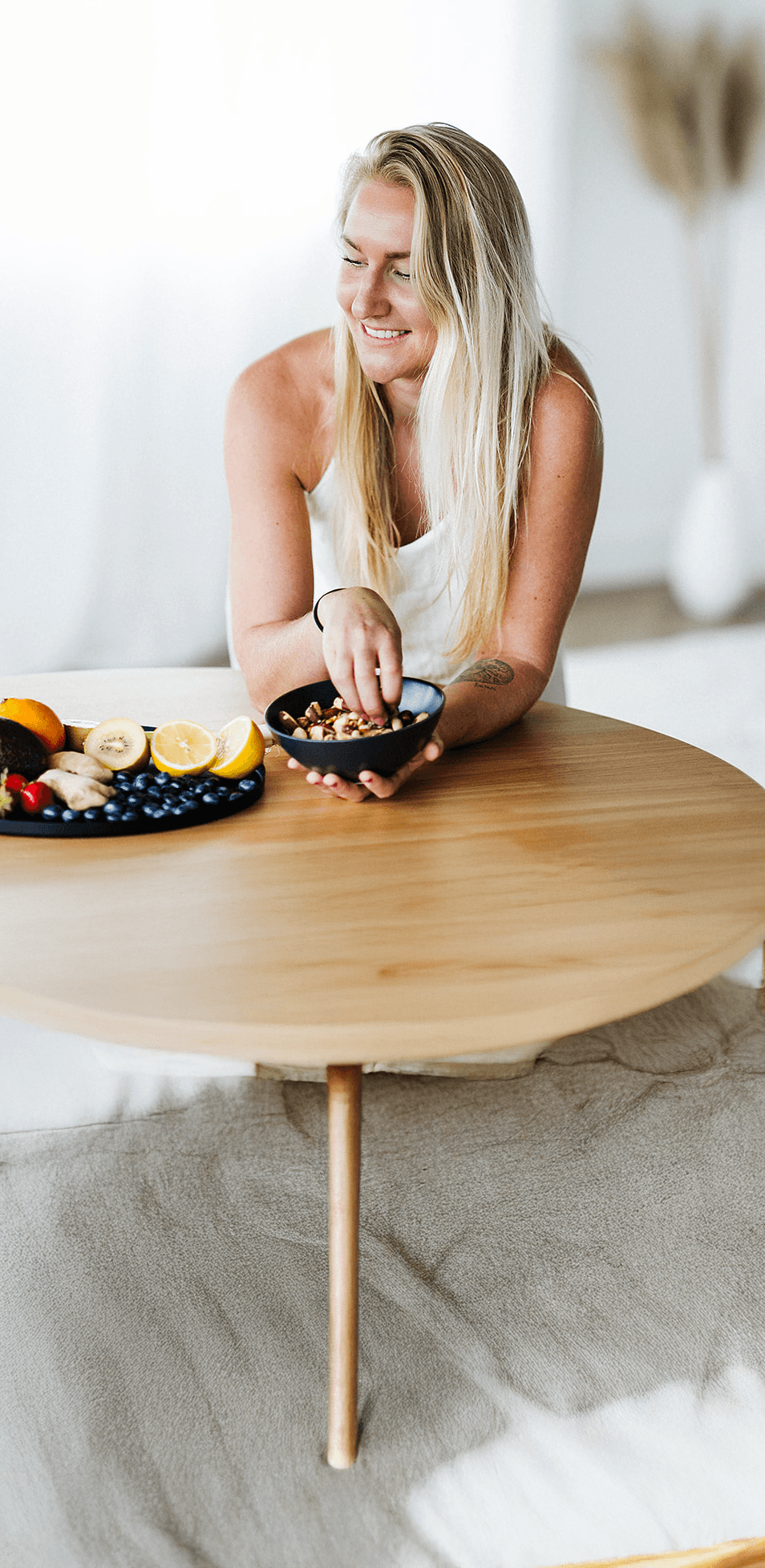 Daphne Medema van Hormone Healing Hub glimlachend met een schaal noten en vers fruit, bij de gratis 3-daagse voeding minicursus tegen PMS.