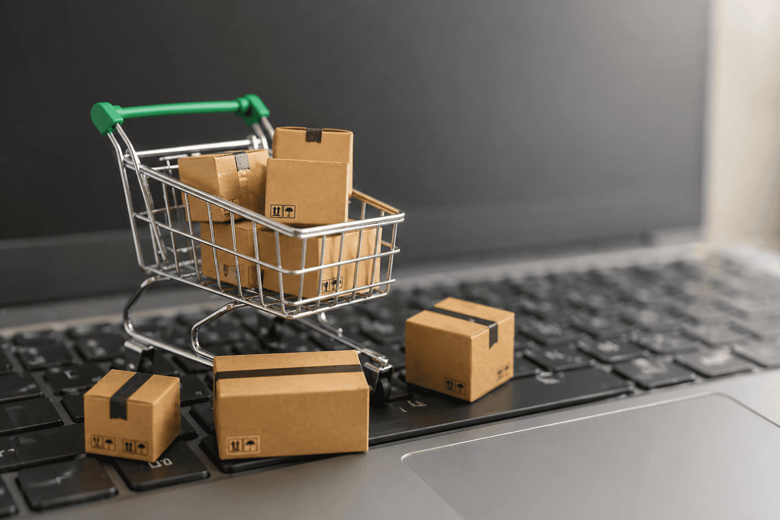 Mini shopping cart with cardboard packages on a laptop keyboard.
