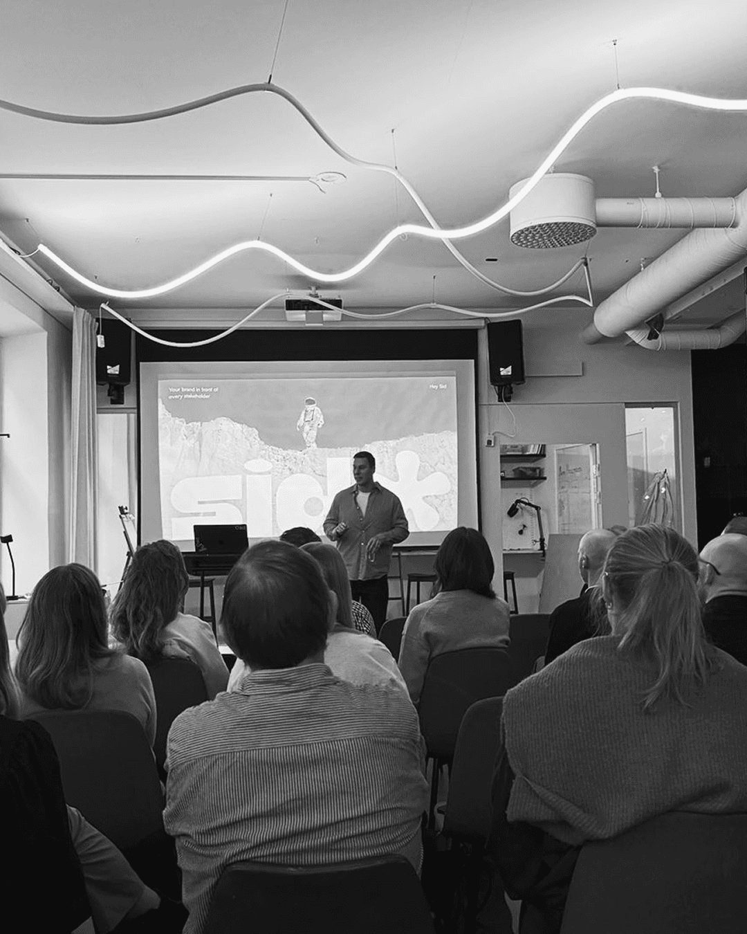 Black-and-white photo of a person standing outdoors in a city square, holding a small cup and spoon.