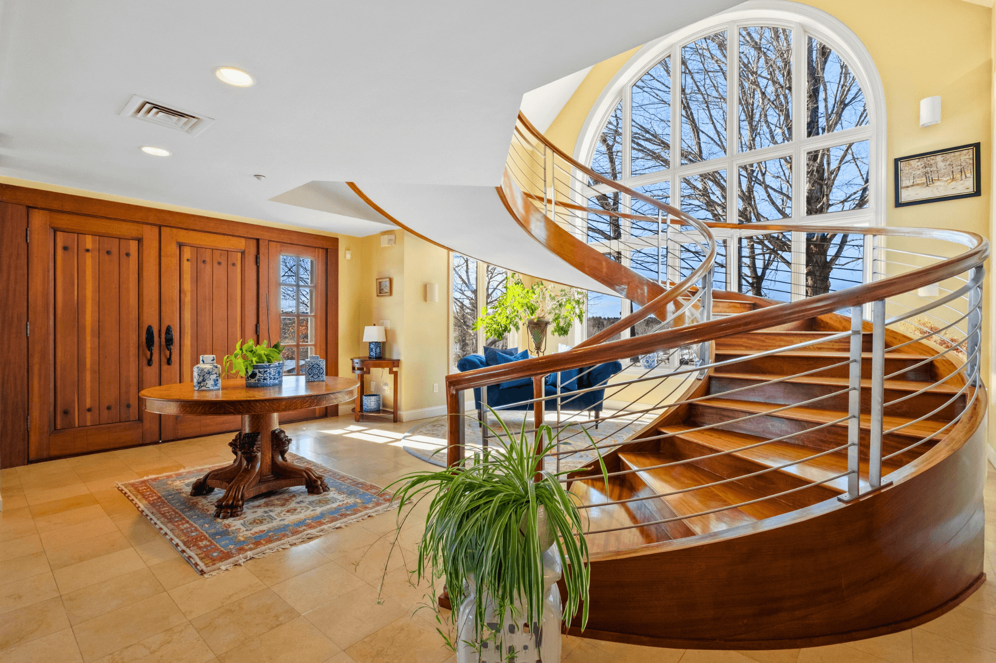Elegant spiral staircase in the grand entry of Meadow View Manor, featuring natural light from arched windows and upscale design details—perfect for luxury Airbnb experiences or retreats.