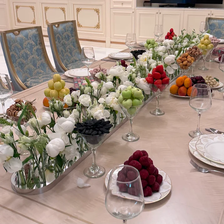 Luxurious dining table with white flowers, assorted fruits, and ornate blue and gold chairs