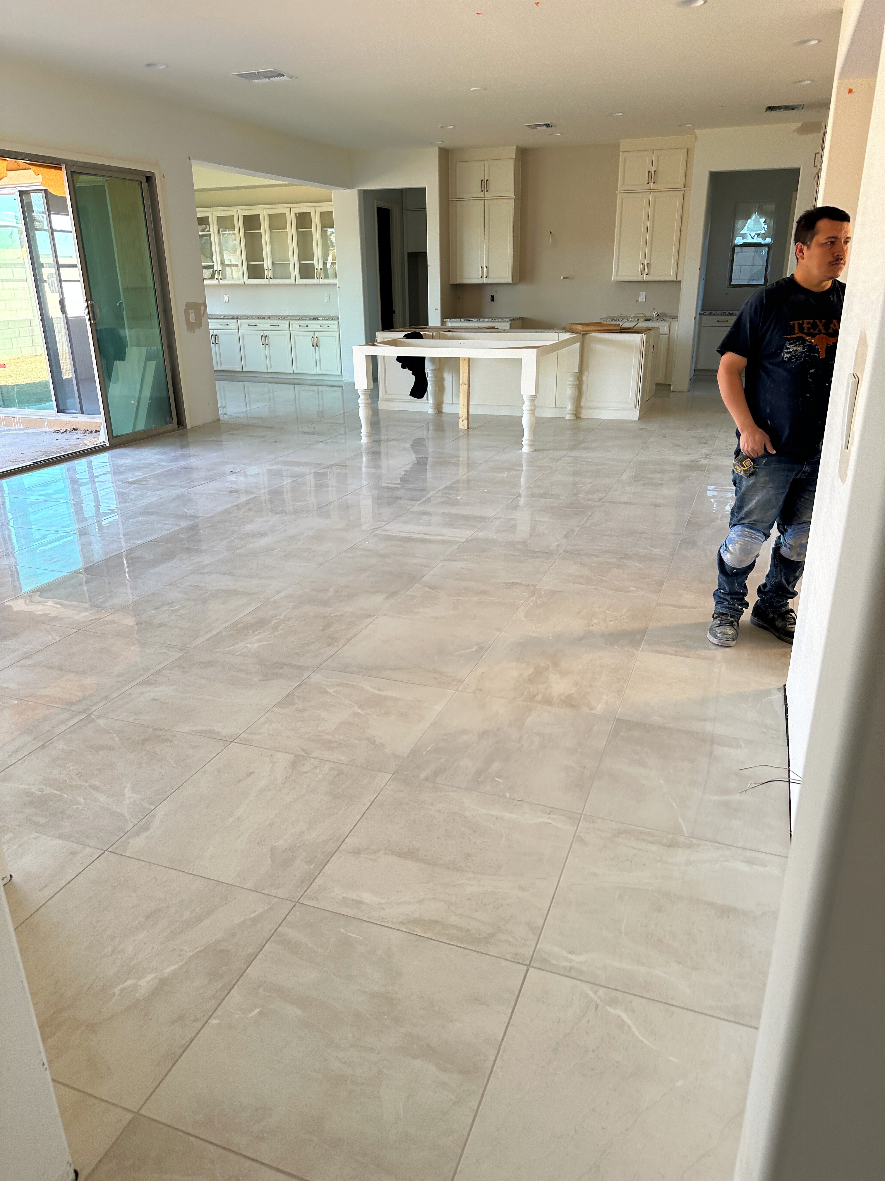 Modern living area with glossy marble tiles, white cabinets, and a worker, featuring large sliding glass doors in a new home.