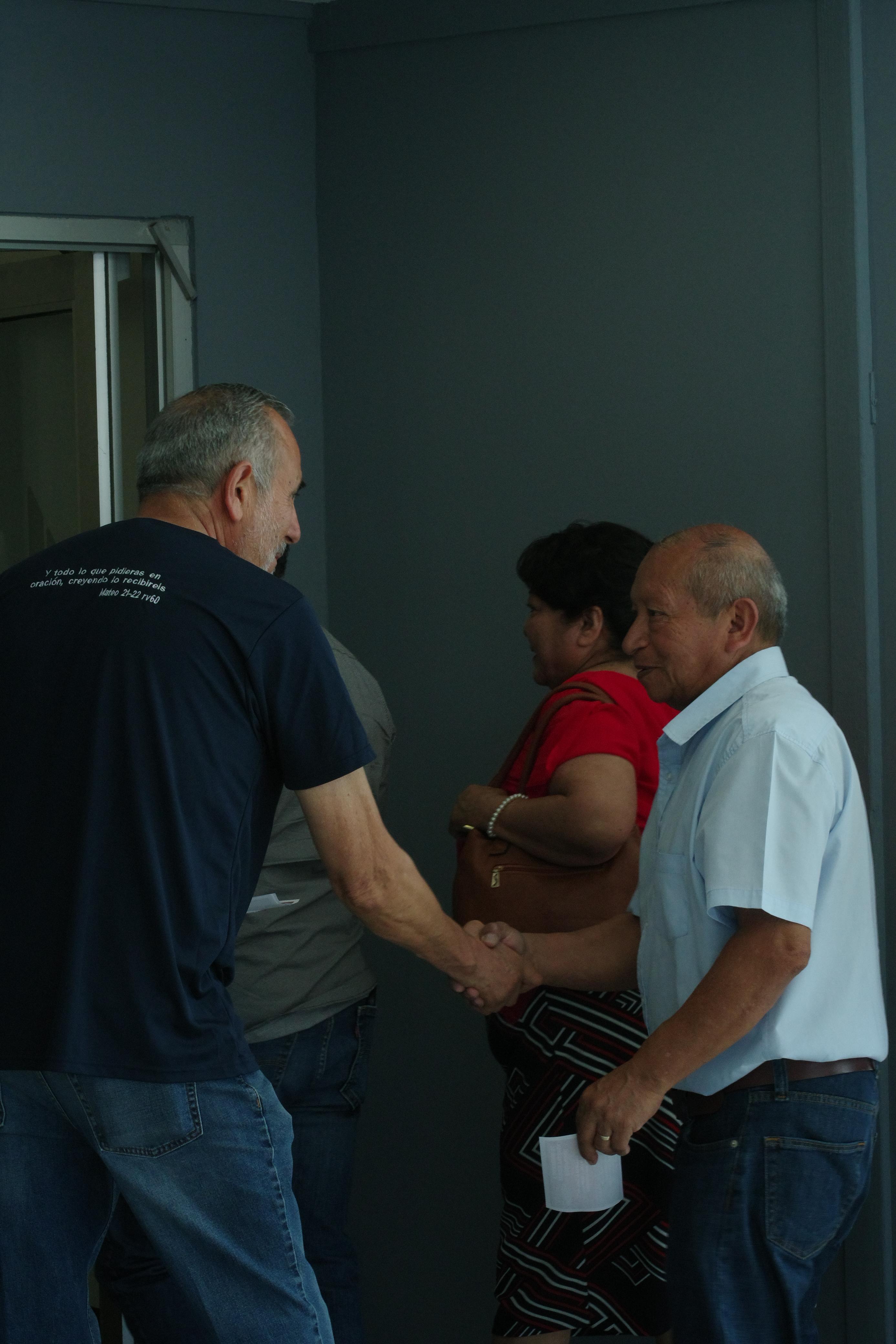 A group of people sitting on grass under trees, enjoying a sunny day near a body of water.