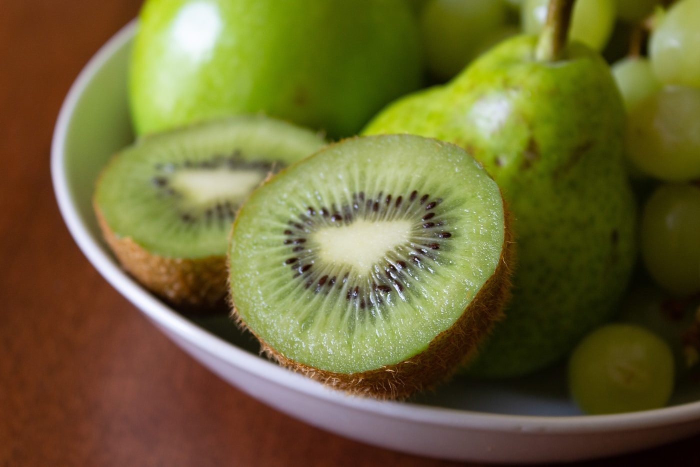 A white bowl of sliced kiwi with pears and grapes, high-fiber fruits that help relieve constipation