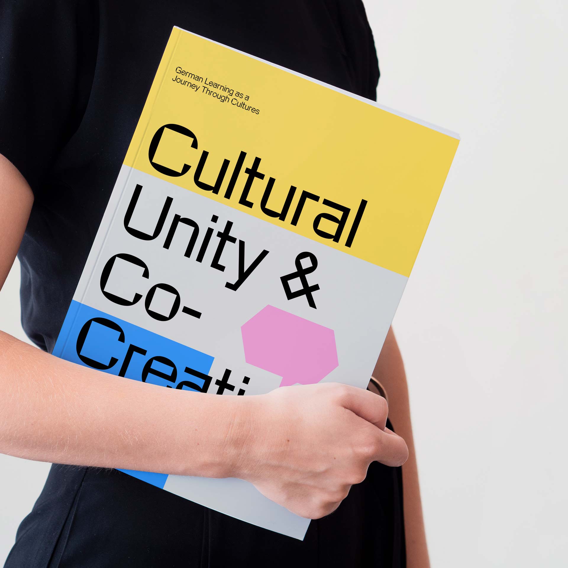 Person holding a book titled 'Cultural Unity & Co-Creation' with a yellow, pink, blue cover