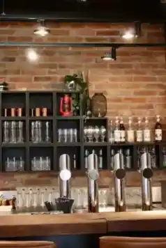 Barbereich im kAlps mit Zapfanlagen, Gläsern, Spirituosenflaschen und Backsteinwand.