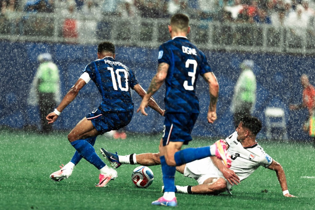 Kylian Mbappé drives forward as an Iraq defender slides in during a rain-soaked World Cup clash