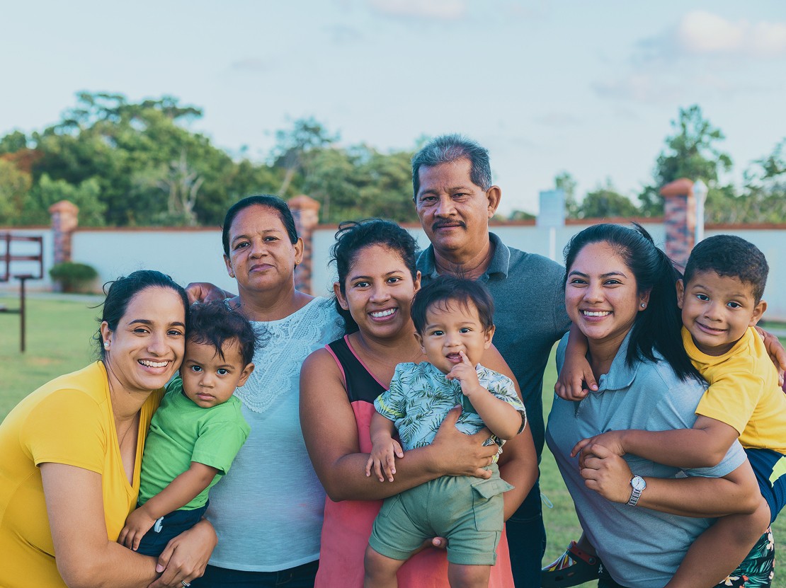 A large, diverse, and smiling multigenerational family group posing together outdoors with several adults and young children