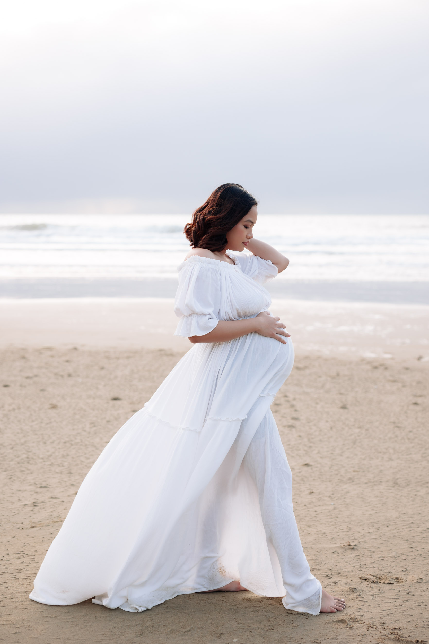 Pregnant women holding baby bump on the beach at maternity photography session in Makay