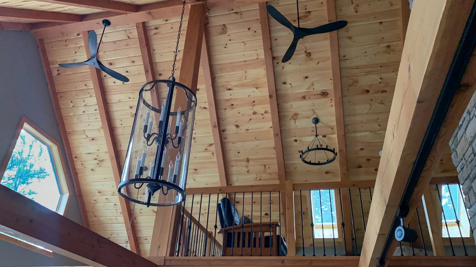 Vaulted ceiling with exposed timber beams and hanging lights with a loft style room on second floor.