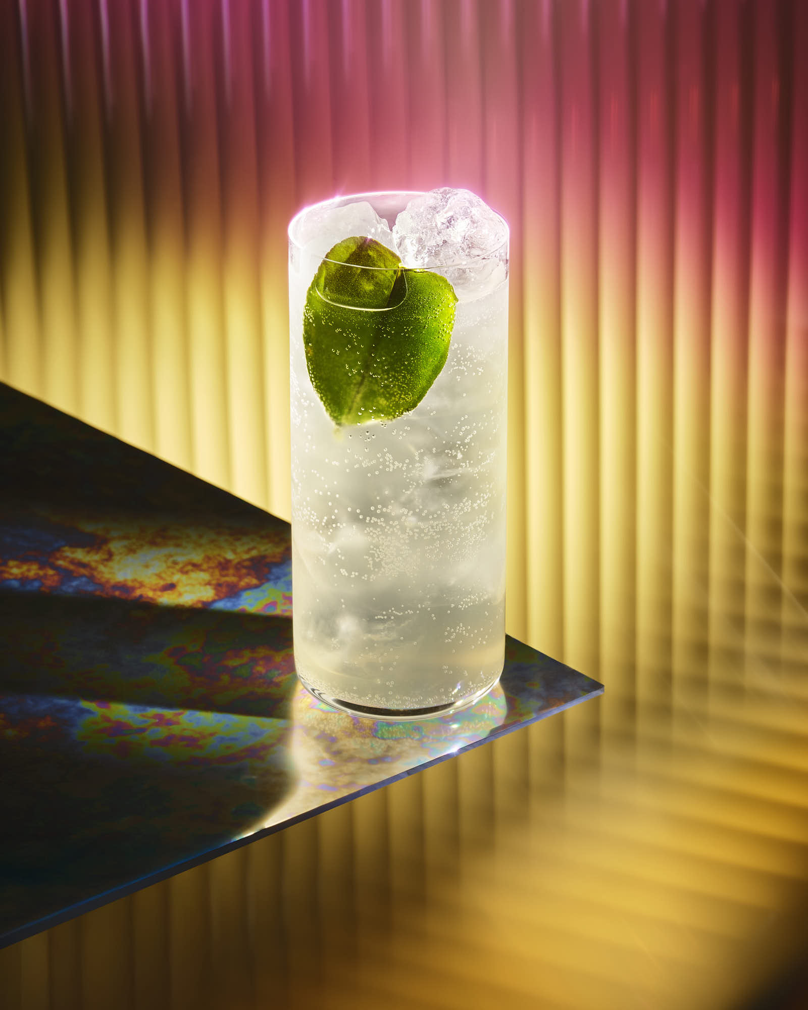 A glass of cocktail with ice and a lime garnish against a colorful background.