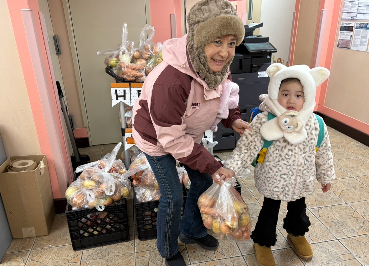 A senior and a young student picking up a bag of autumnal produce. 