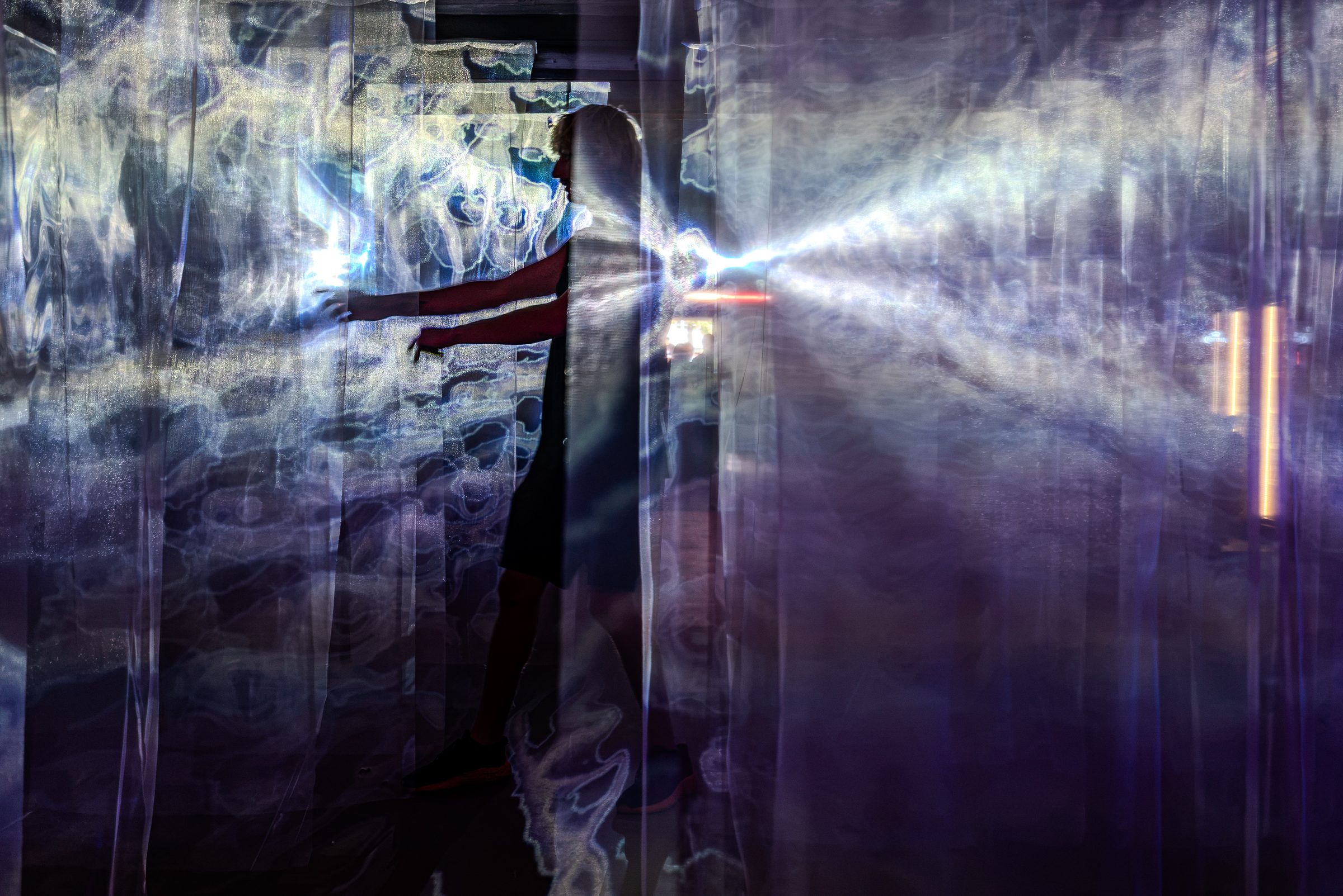 A person reaching out between the curtains, light rays projected across the fabric