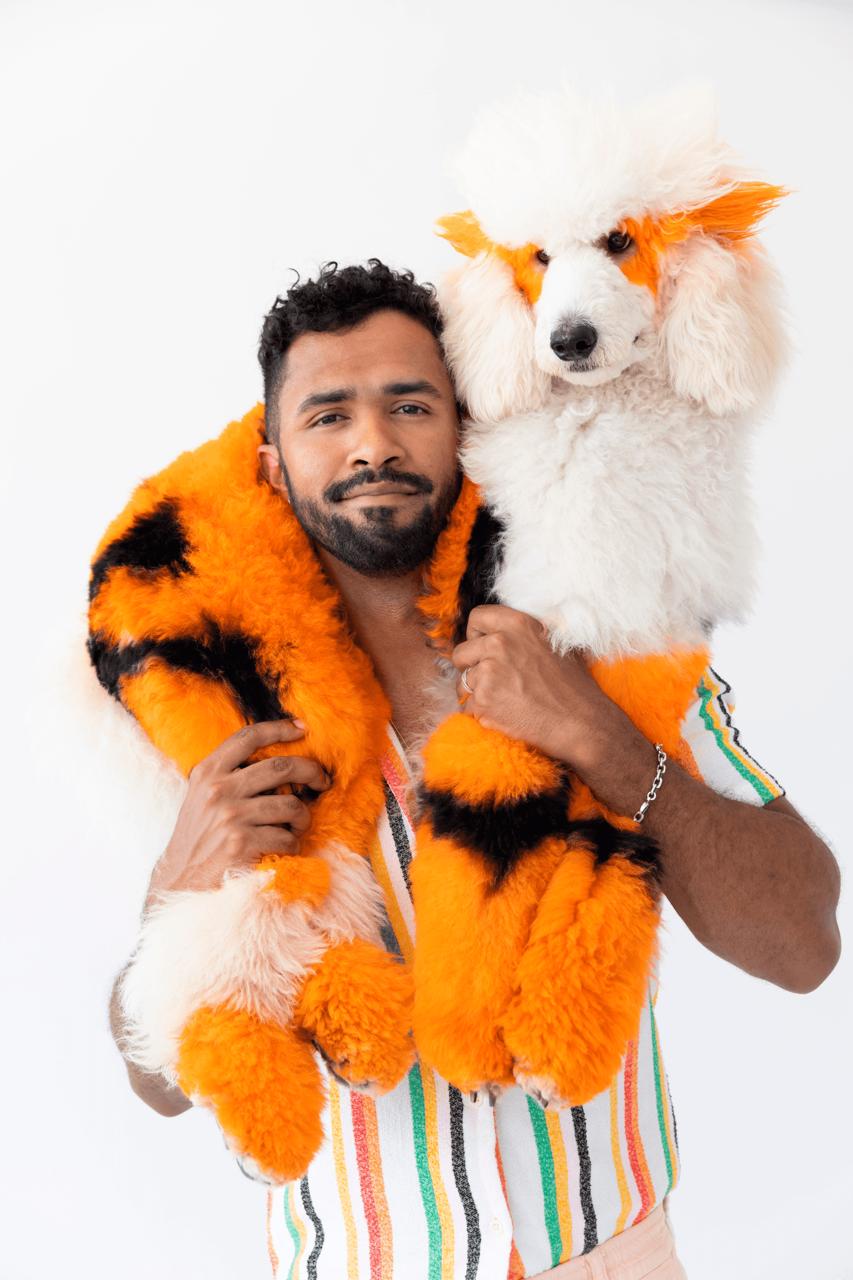 Vibrant portrait of Gabriel Feitosa holding a creatively styled poodle with orange and black accents to express bold artistry and joyful luxury in pet grooming.