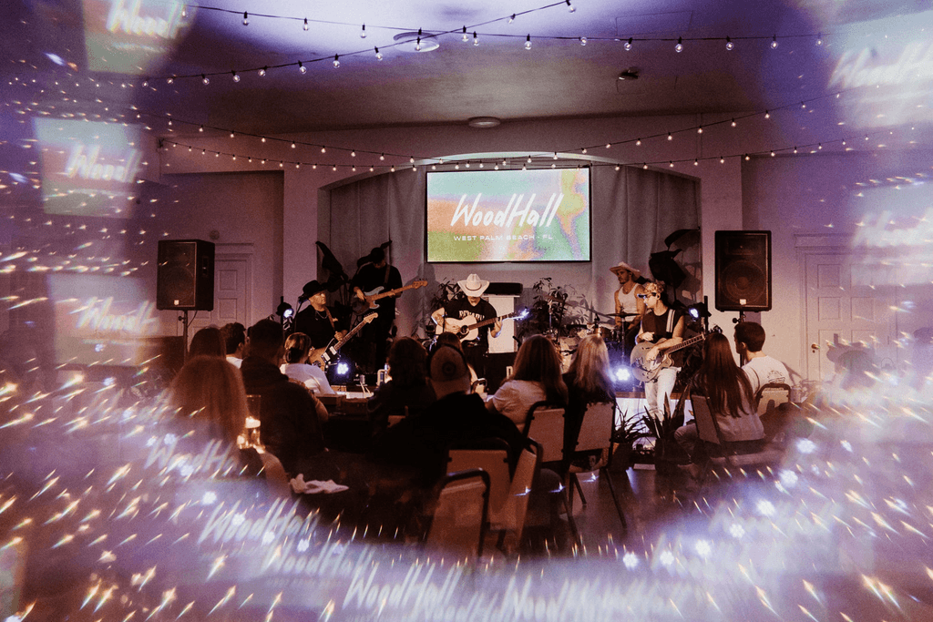 A speaker on stage, illuminated against a dark background, gestures while addressing an audience.