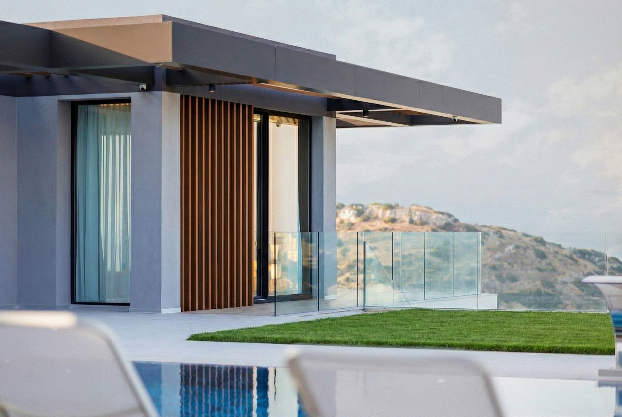 Modern villa terrace with glass balustrade, vertical timber screens, and mountain views