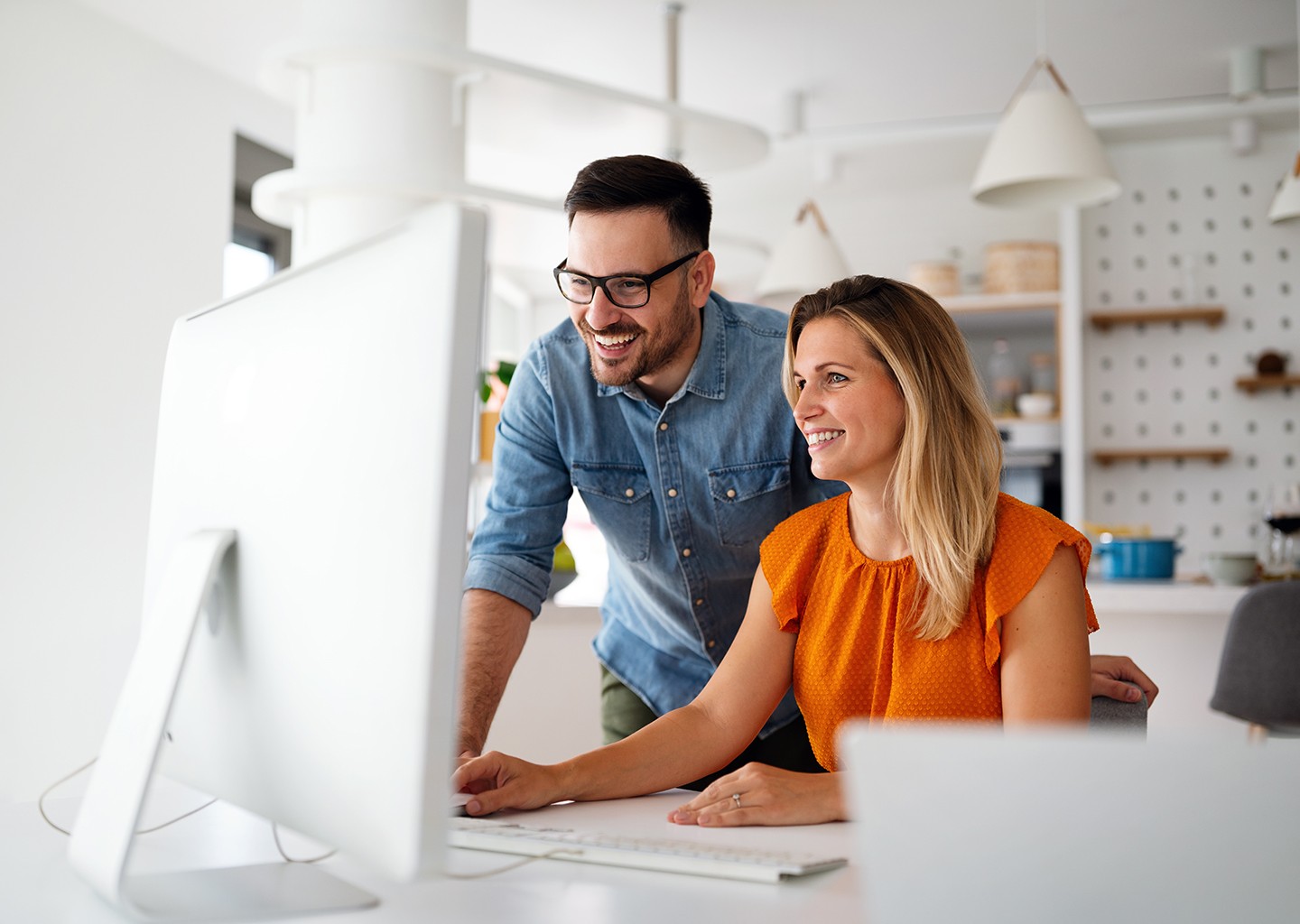 Due colleghi sorridenti che consultano insieme il calendario delle presenze su uno schermo, rappresentano la flessibilità lavorativa offerta dalla banca ore.