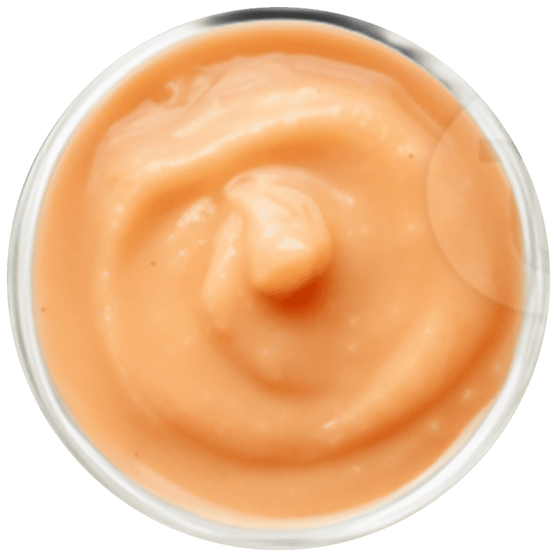 A bright, modern dining room featuring a long light wood table set with several matching wooden chairs and white cushions, illuminated by natural light streaming through large windows overlooking a lush green and sunlit yard.