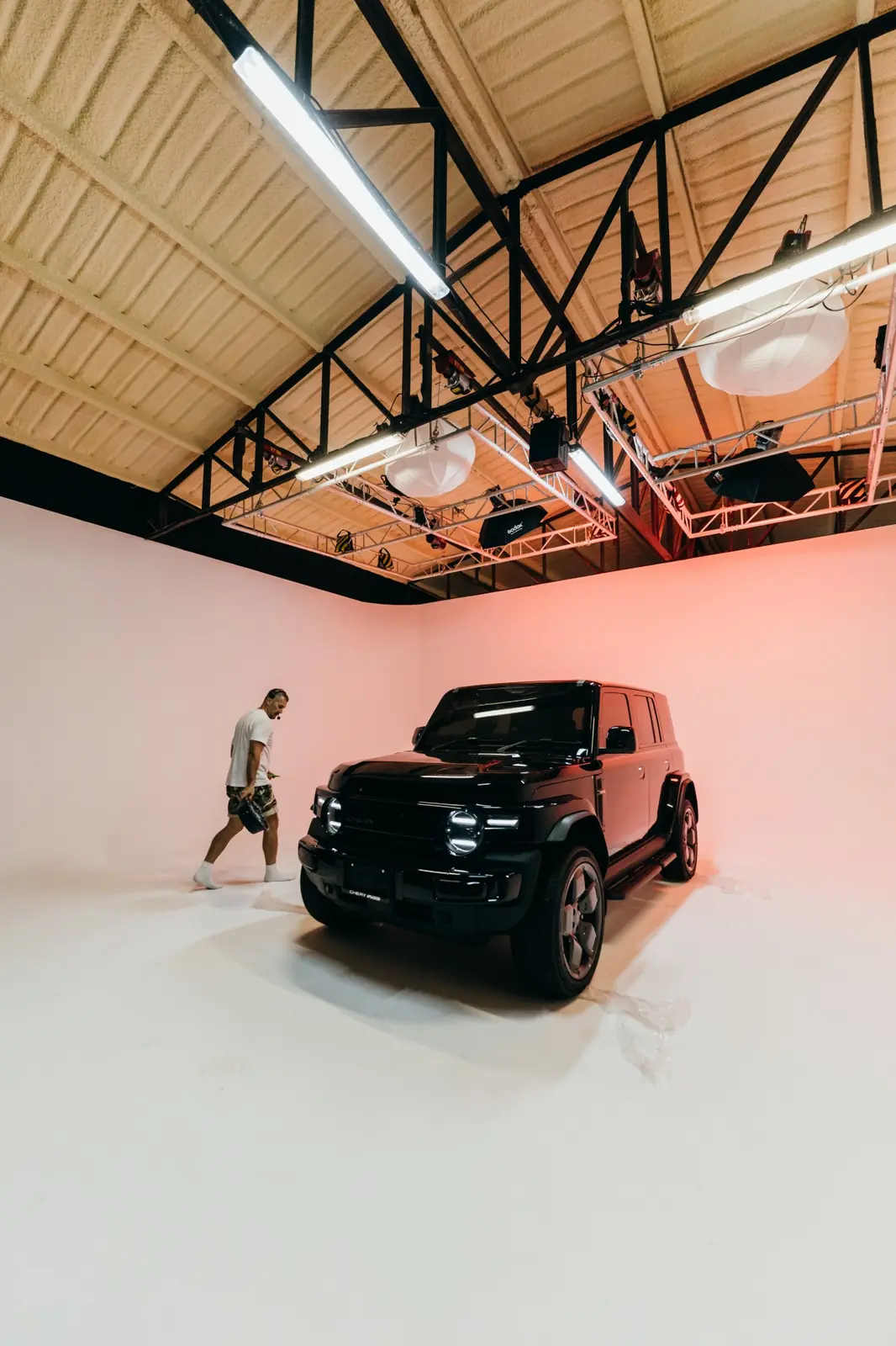Crew member walking past the Chery V23 on the white cyclorama, with protective film by the tires