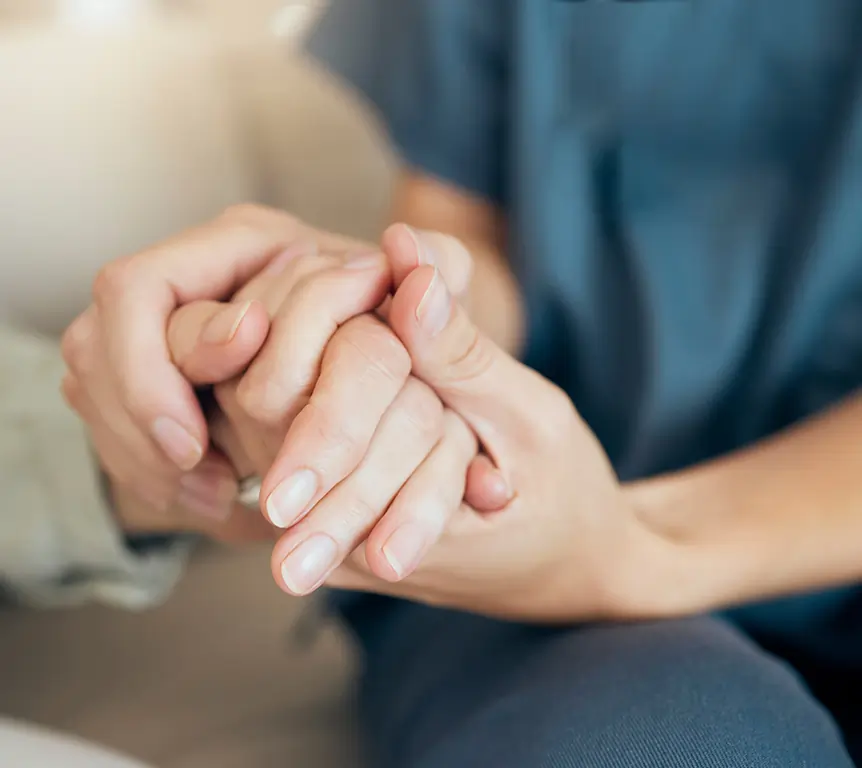 Caregiver gently holding the hand of a senior during hospice and comfort care