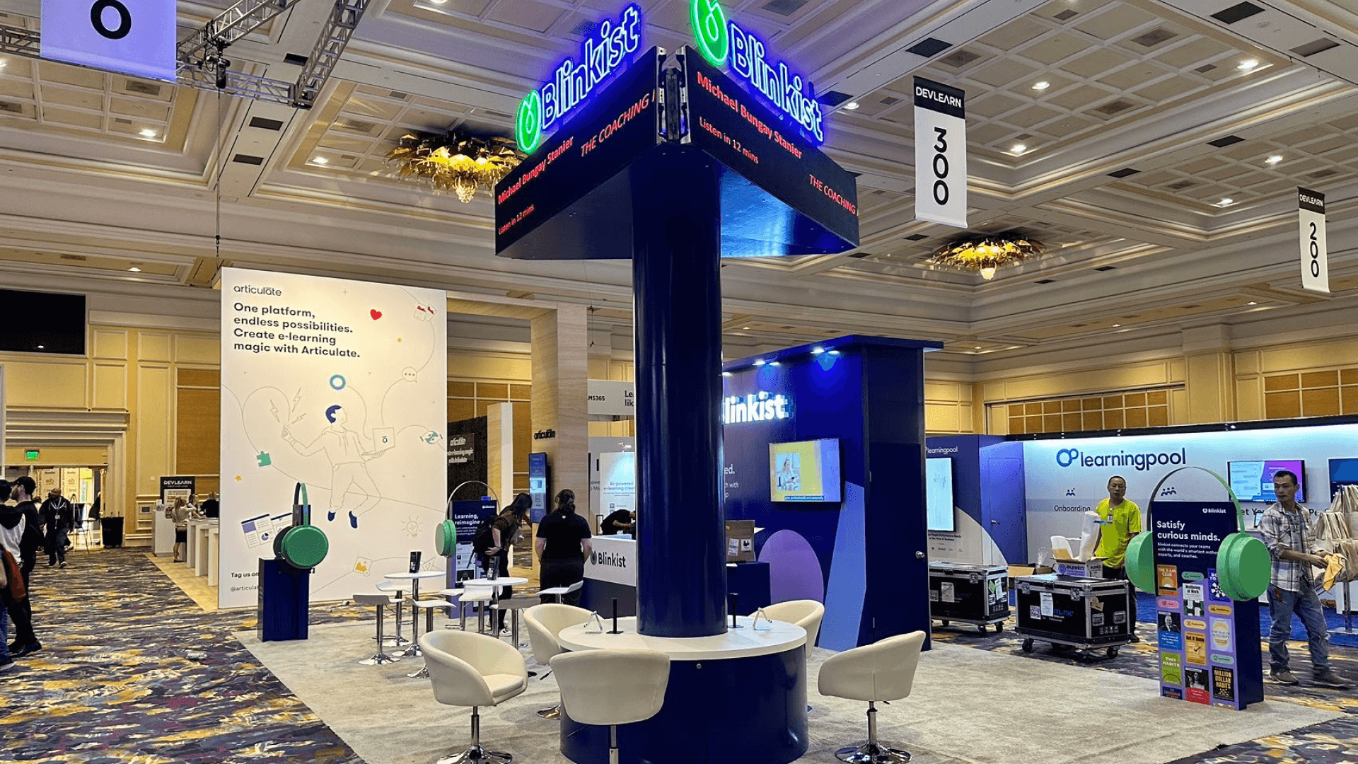 Blinkist DevLearn Conference & Expo 2025 20x40 technology product demo booth with elevated digital signage tower, branded wall graphics, visitor seating, and open aisle-facing layout
