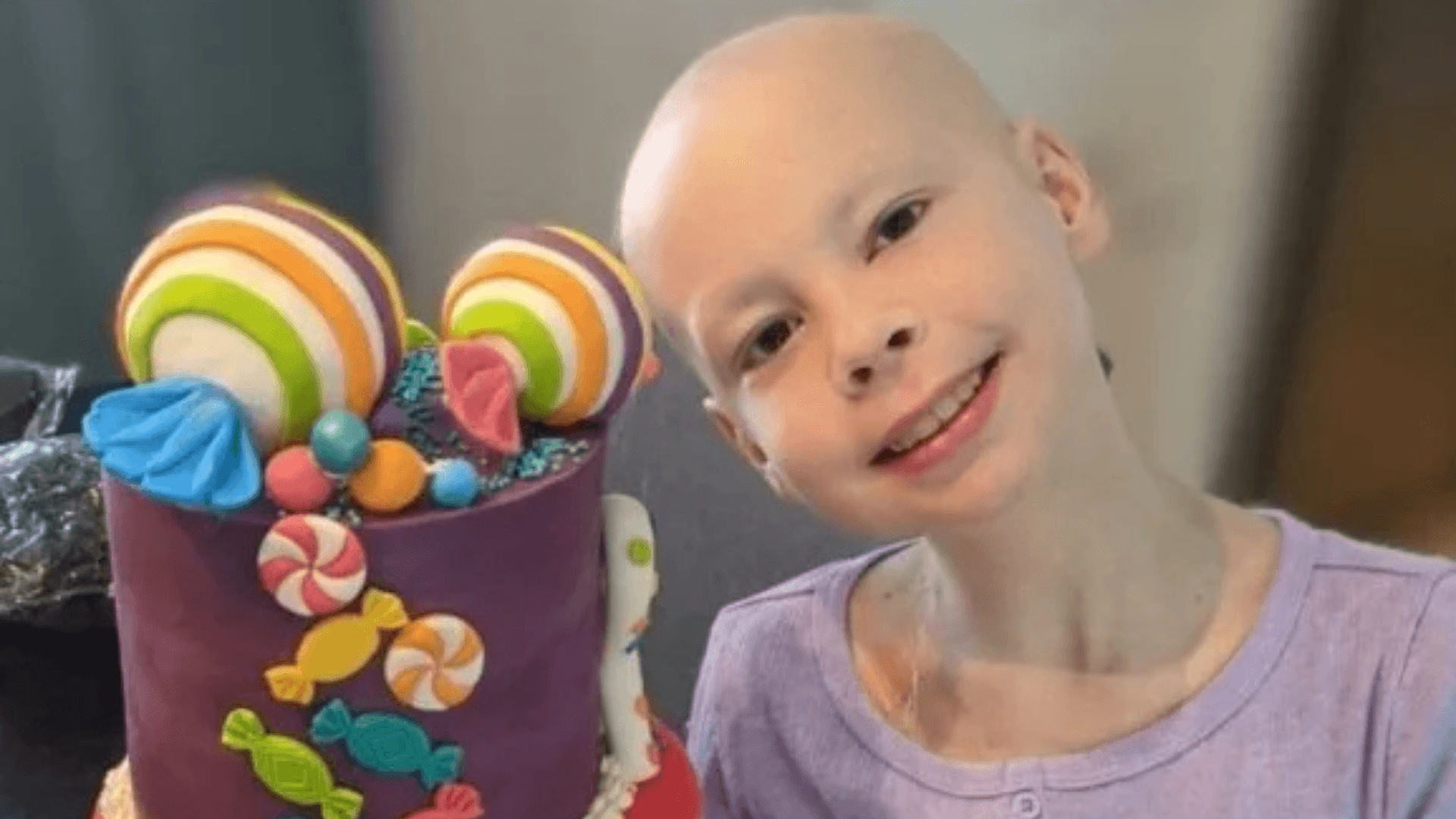 Alt tag: Smiling child with a bald head holding a colorful candy-themed craft container, posing indoors