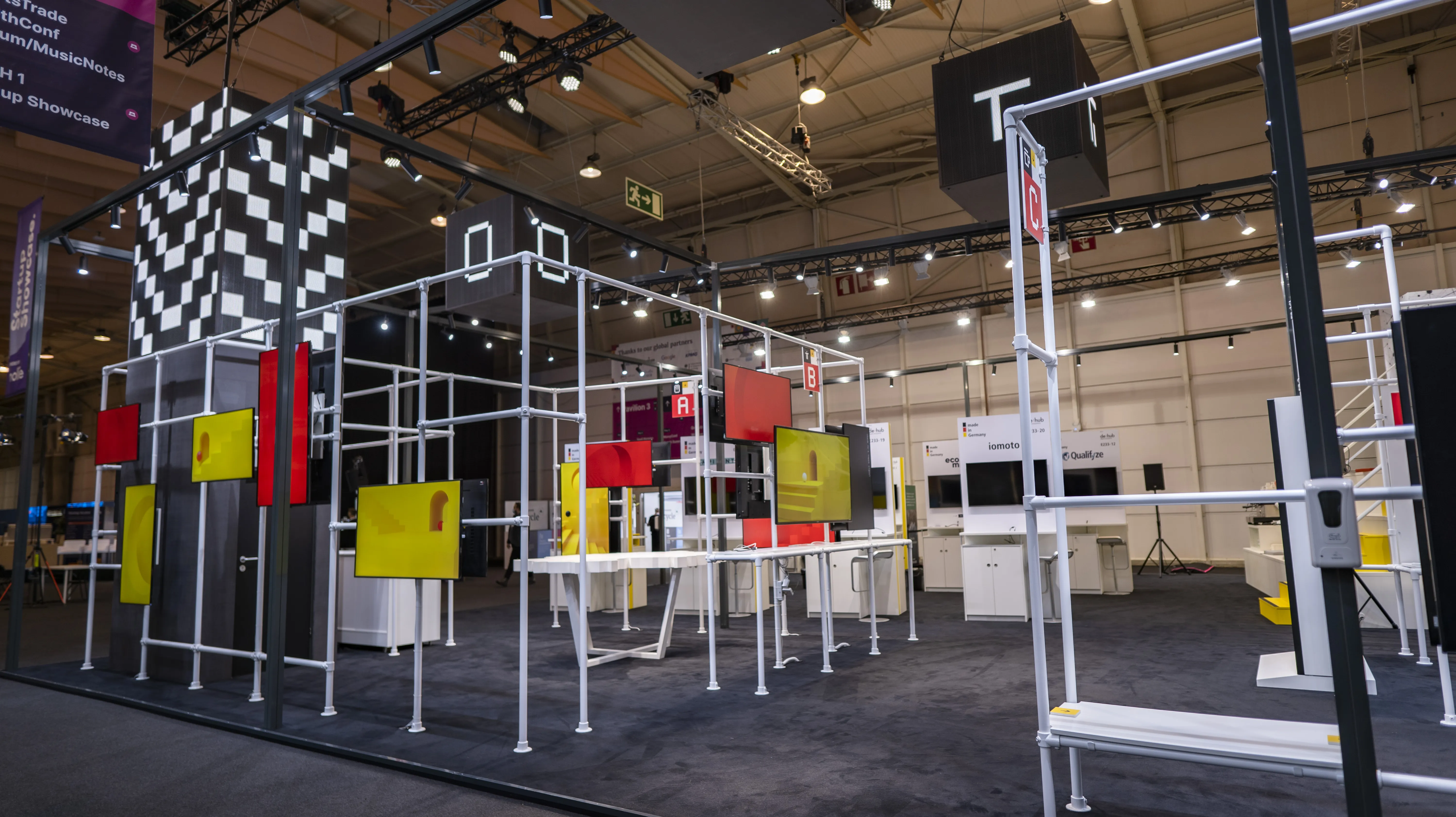 White modular frame system of the German Pavilion with red and yellow displays and a black-and-white checkered tower.