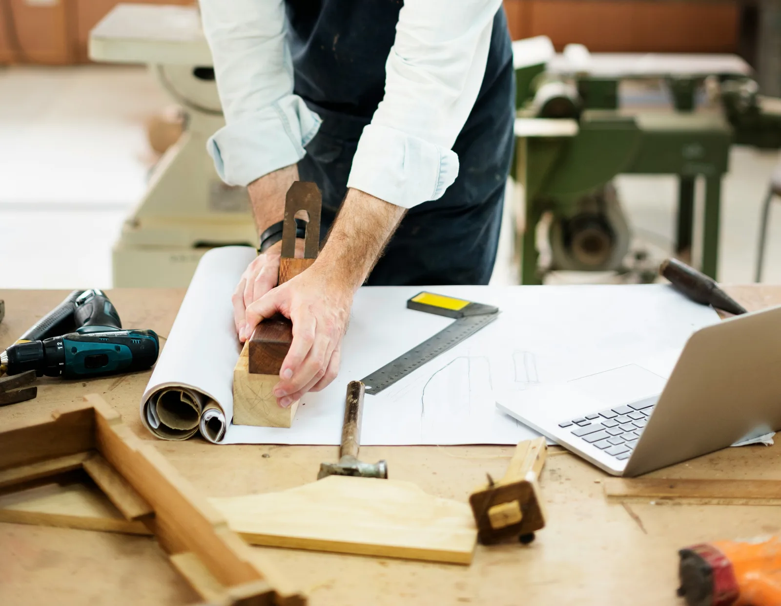 Майстор измерва дървен детайл с инструменти и чертежи на маса