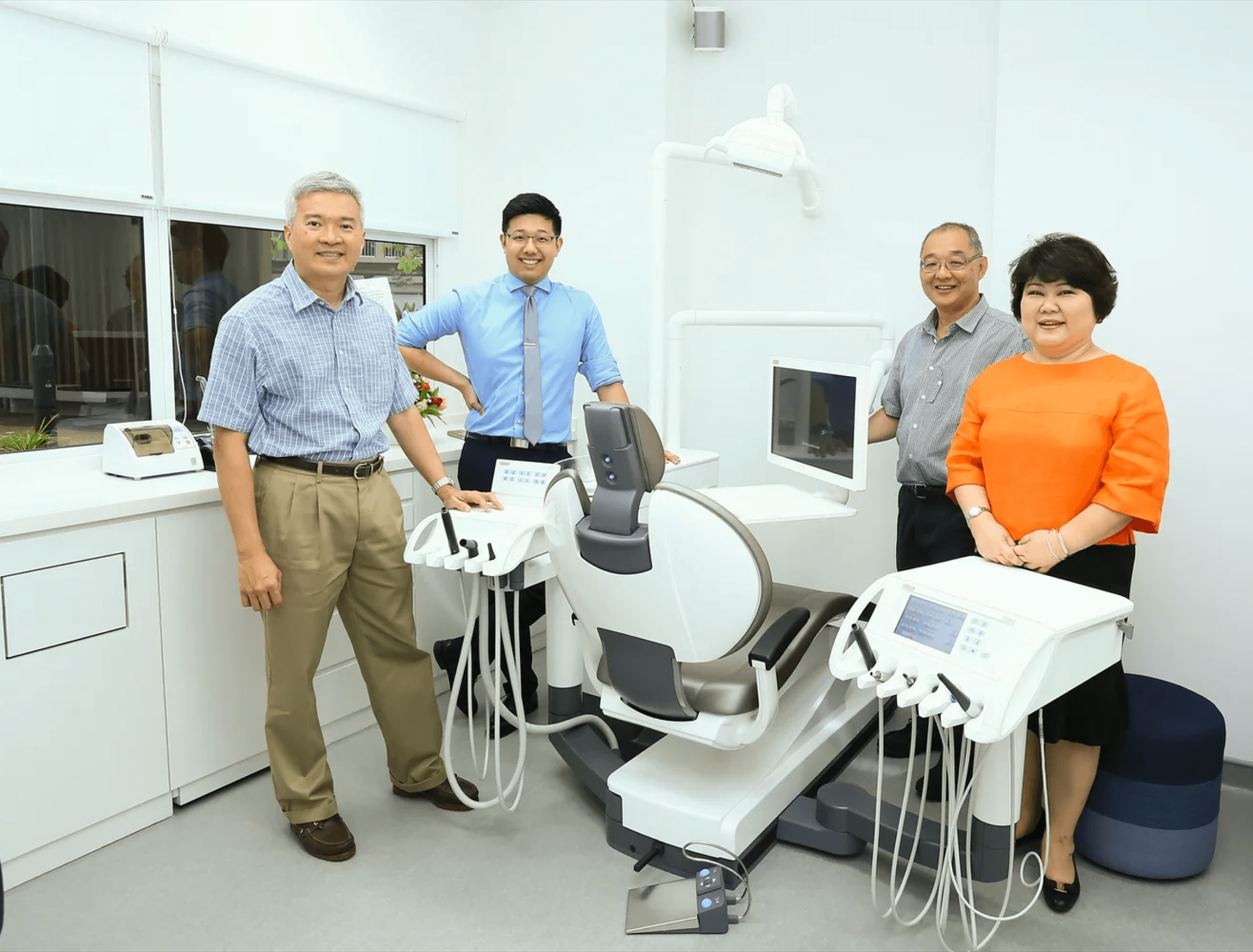 A group of four people stands in a modern dental clinic, featuring advanced dental equipment and a comfortable dentist chair, situated in a bright, sterile environment.