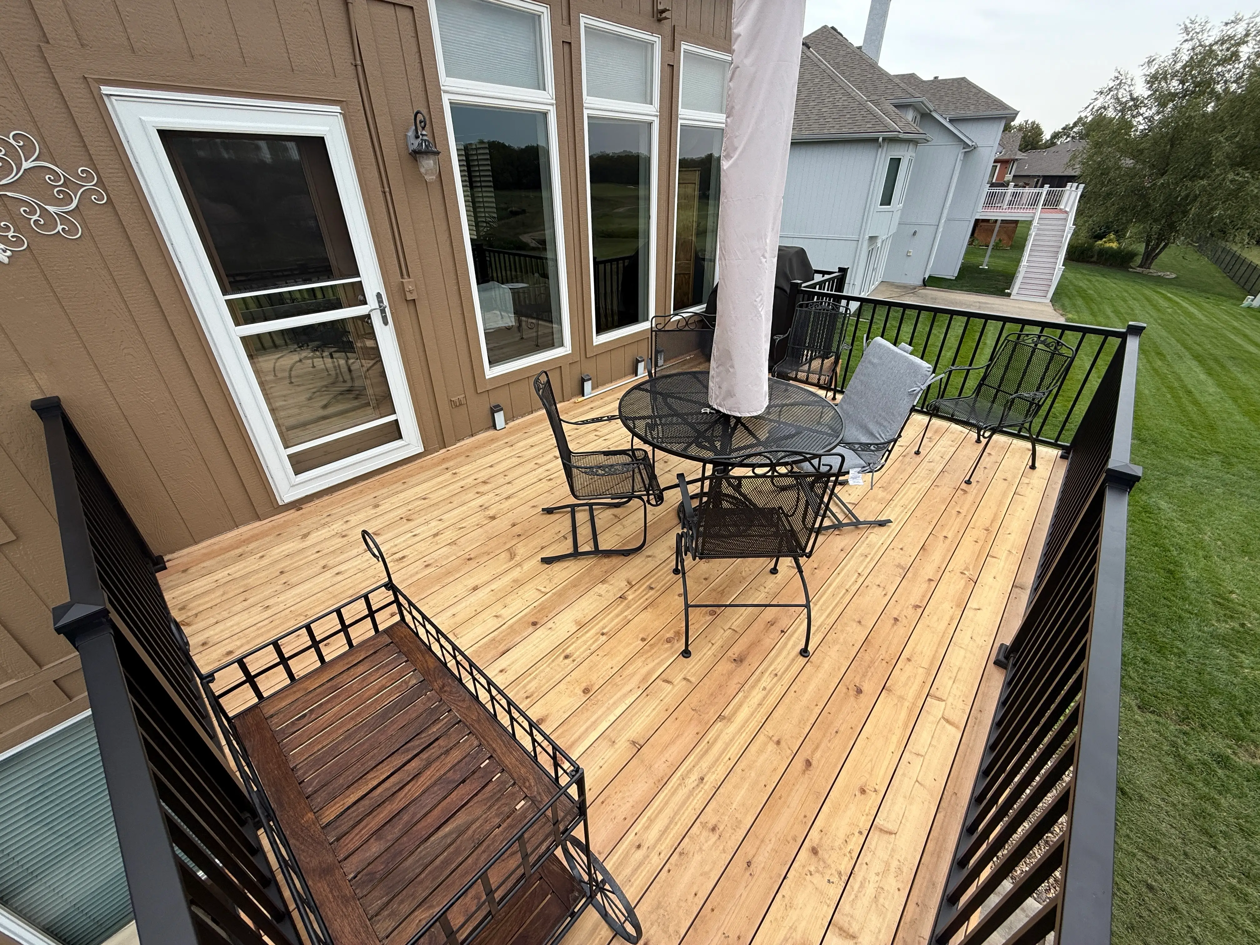 An image of a newly installed natural wood deck against a brown house.