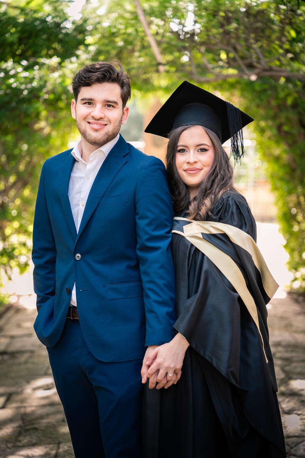 A couple stands on a sandy hill at sunset, facing away, with arms raised in a relaxed "hang loose" gesture. The scene conveys tranquility and joy.